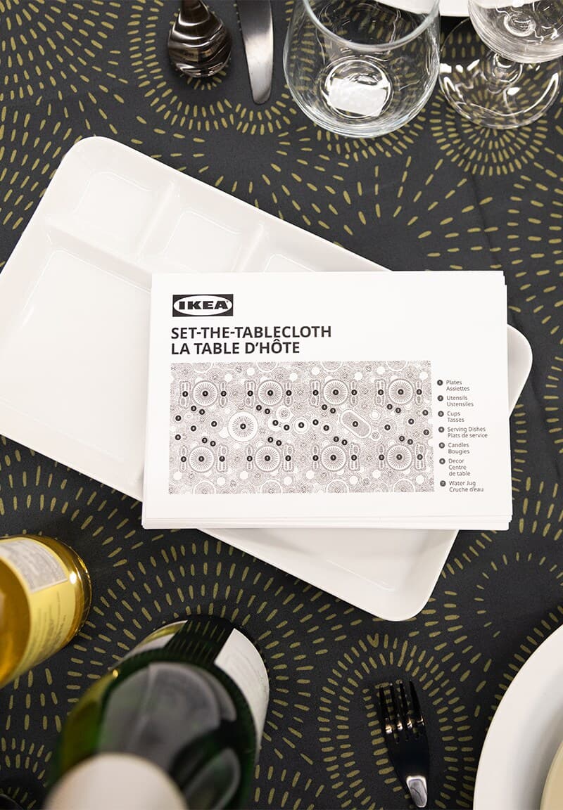 Vue en plongée sur un mode d’emploi de la nappe La table d’hôte IKEA déposé sur une table dressée.