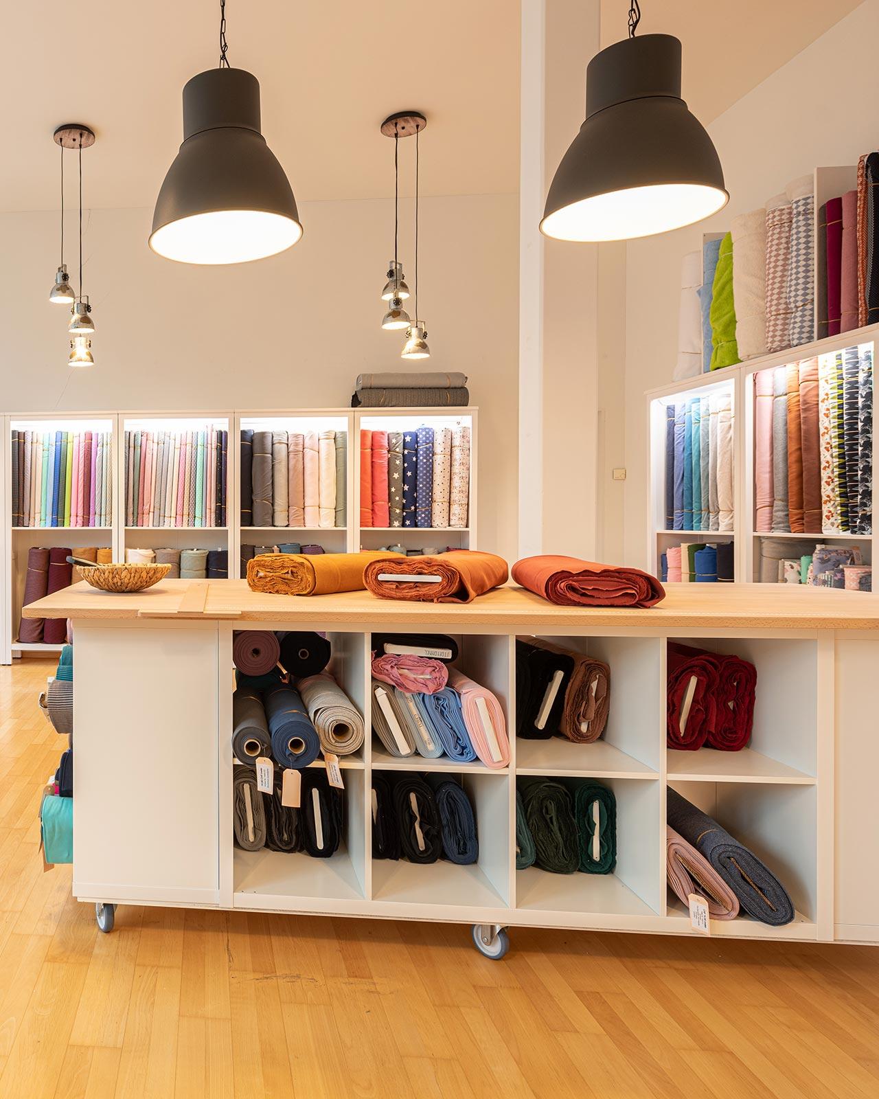 Vue intérieure d’un magasin de tissu avec une grande table de coupe au centre et de nombreuses étagères de rangement pour les tissus