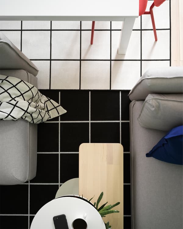 Vue plongeante sur deux tapis à carreaux noirs et blancs, une table de salle à manger blanche et un canapé gris.