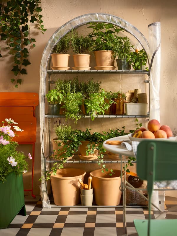 Vysoký skleník ASPAREN stojí na balkóne, pred ním je skladací stolík a stolička SUNDSÖ.