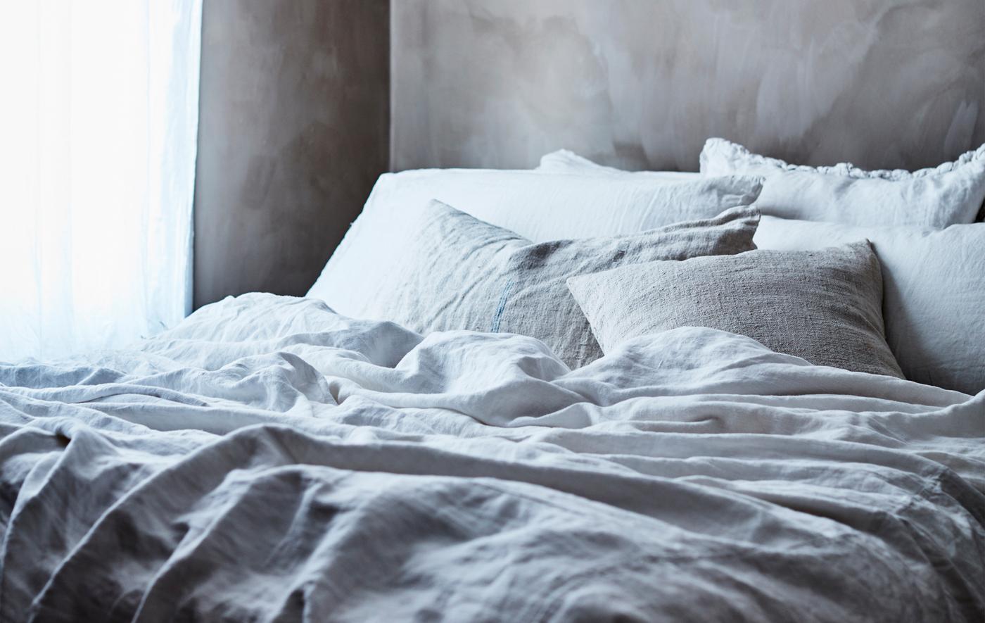Vytvorte útulnú posteľ s vrstvami mäkkých sivo-bielych posteľných obliečok.