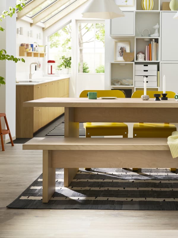 W jasnej jadalni znajduje się stół BERGSHYTTAN z ławką z forniru brzozowego po jednej stronie i kolorowymi krzesłami po drugiej.