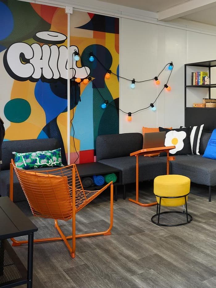 W kolorowych wnętrzu stoi pomarańczowy fotel i żółte siedzisko.