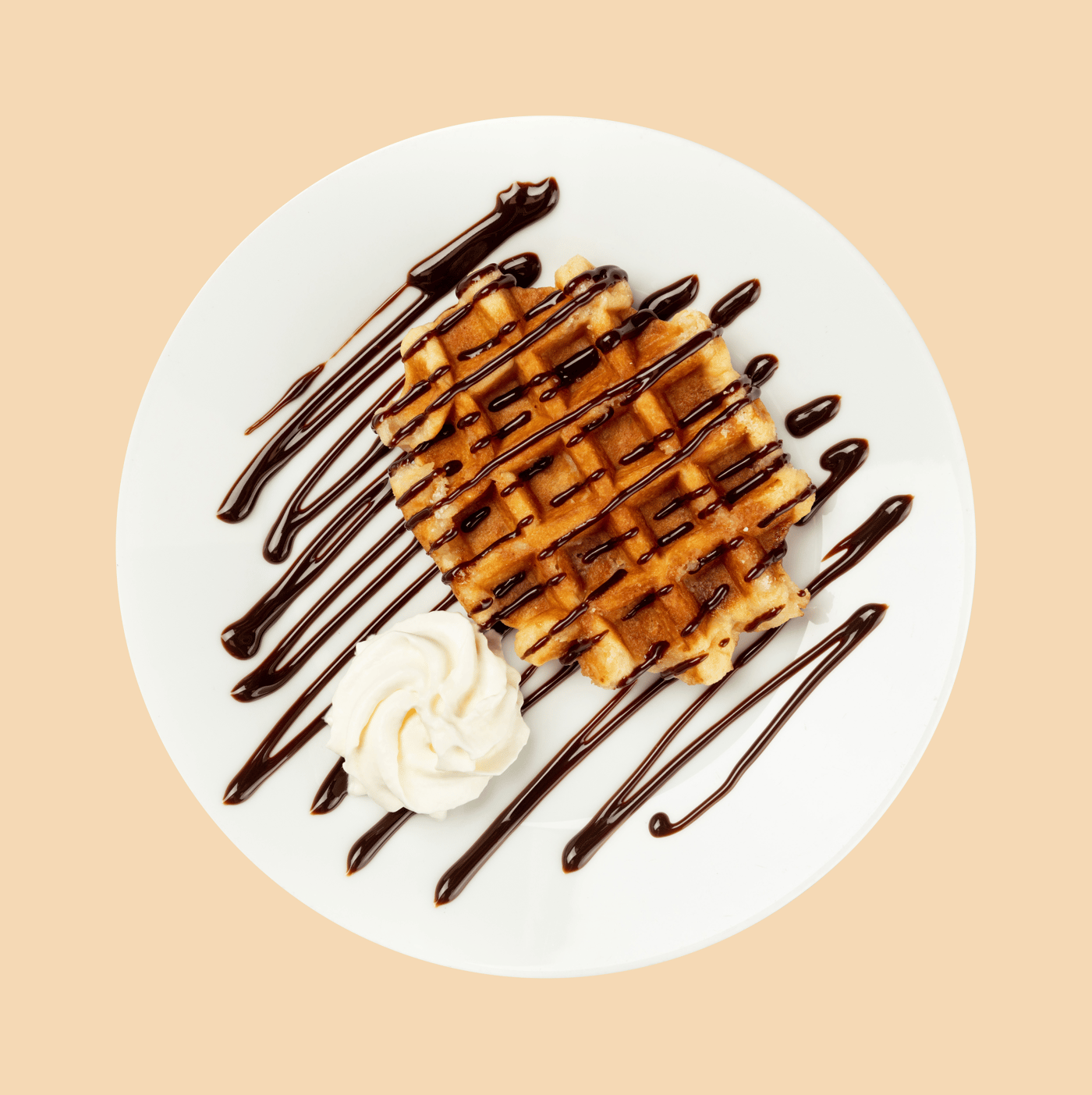 Waffle with cream and chocolate syrup served on a white plate on a beige surface.