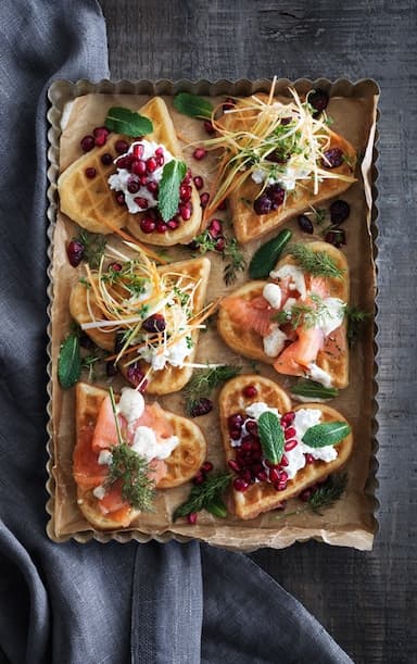 Waffles with various toppings, such as marinated salmon, dried lingonberries with a mix of cress, leek and carrots and pomegranate seeds mixed with cottage cheese.