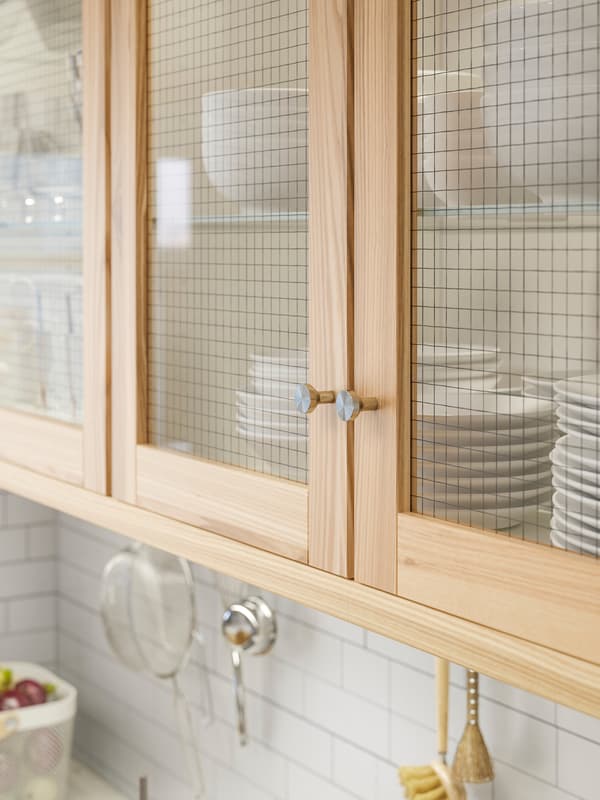 Wall cabinets with ash and glass TORHAMN doors that store white tableware.