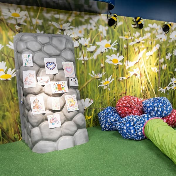 Wall decorated like a stone surface with children’s drawings pinned on it, surrounded by colourful bean bags.
