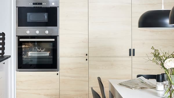 Wall-mounted IKEA METOD kitchen cabinets with ASKERSUND doors in light ash wood effect and a built-in oven and microwave.