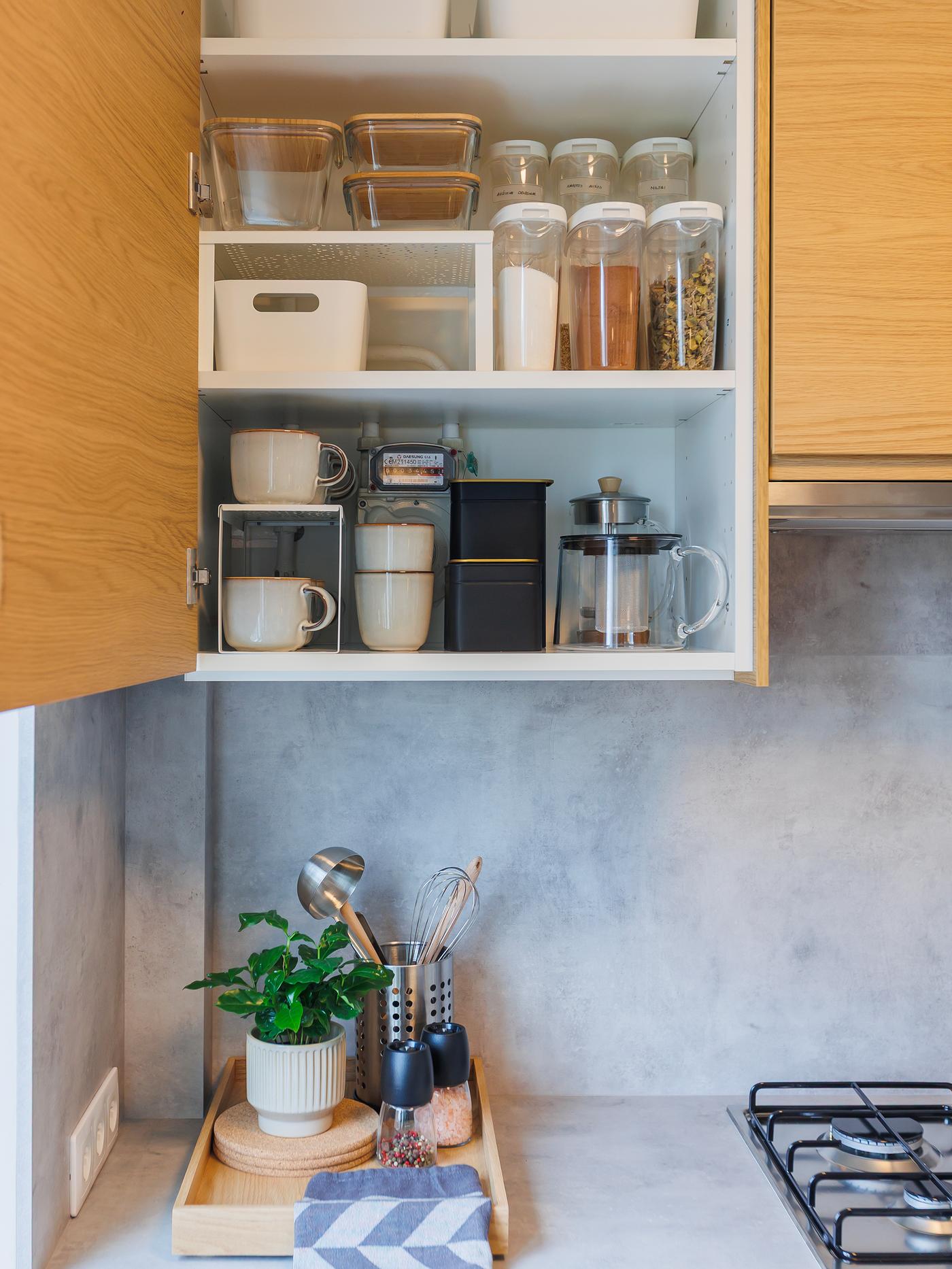 Wall-mounted kitchen cabinet with an open door, neatly storing jars, containers and other kitchen essentials above the worktop.