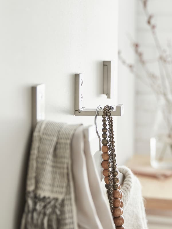 Wall section with BJÄRNUM hooks, two of which hold clothes and accessories.