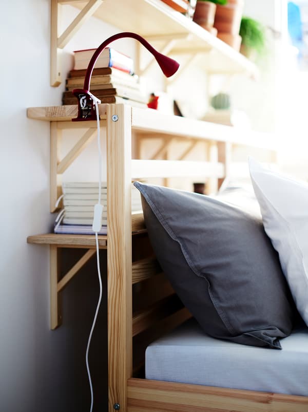 Wall shelves fill the space between a wall and the head end of a bed, creating a combination of storage and bedside table.