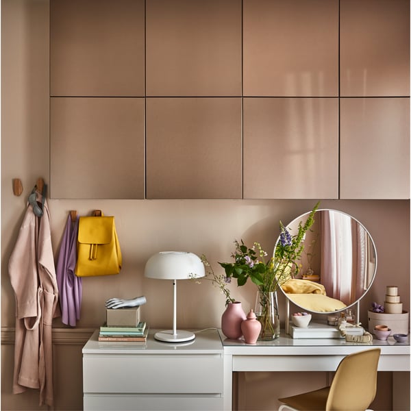 Wandkastdeuren met licht bronseffect, een witte toilettafel een ronde witte spiegel en wandgemonteerde haken van bamboe.