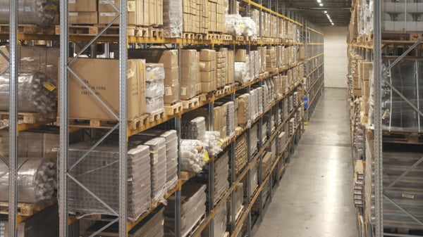 Warehouse aisle with tall shelves stacked with boxes and pallets.