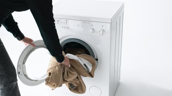 We see a black-sleeved arm putting pale brown textile into a washing machine.