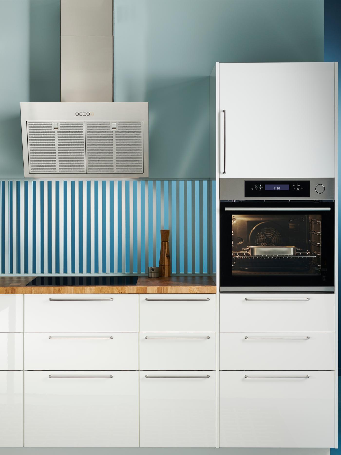 Weiße IKEA-Küche mit Holzarbeitsplatte, Abzugshaube und Backofen mit weißen Fronten und holzerner Arbeitsplatte.