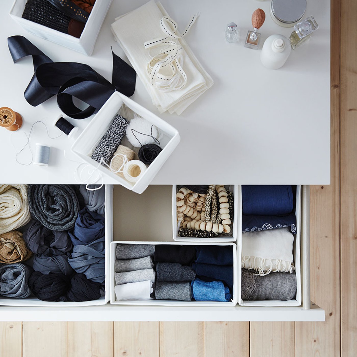 Weisse SKUBB Boxen mit Kleidung und Accessoires stehen auf einer Oberfläche und in einer offenen Schublade einer weissen MALM Kommode.