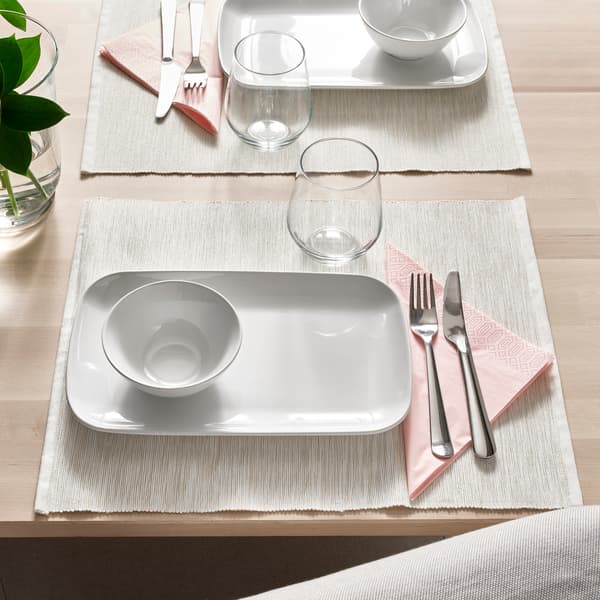Weißer rechteckiger Teller mit runder Schüssel, Glas und Besteck auf Tischset.