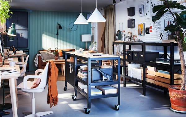 Werkplek met twee BROR zwarte/houten trolleys met opbergers op wielen, twee witte hanglampen en een zwarte lange stellingkast.