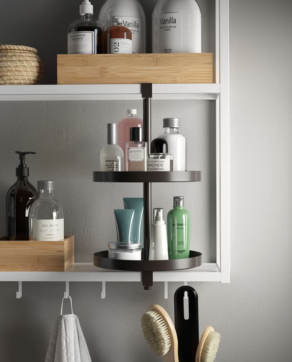 وحدة رفوف بيضاء مع خطافات ورف دوار أسود. صواني وصناديق وعطور ومستحضرات وغيرها على الرفوف.