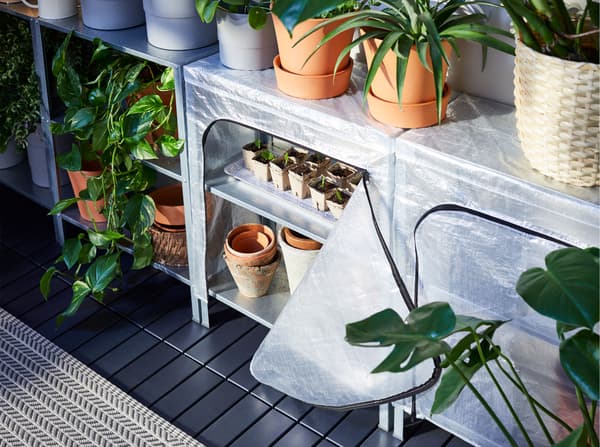 وحدة رفوف HYLLIS من ايكيا، بعضها بأغطية بسحاب، مع أواني نباتات من أعلى وفي الداخل.