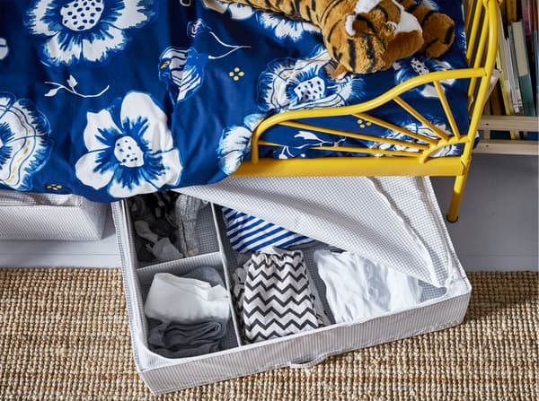 White and grey striped IKEA STUK clothes storage cases, with top zipper, poking out from under a yellow MINNEN bed.