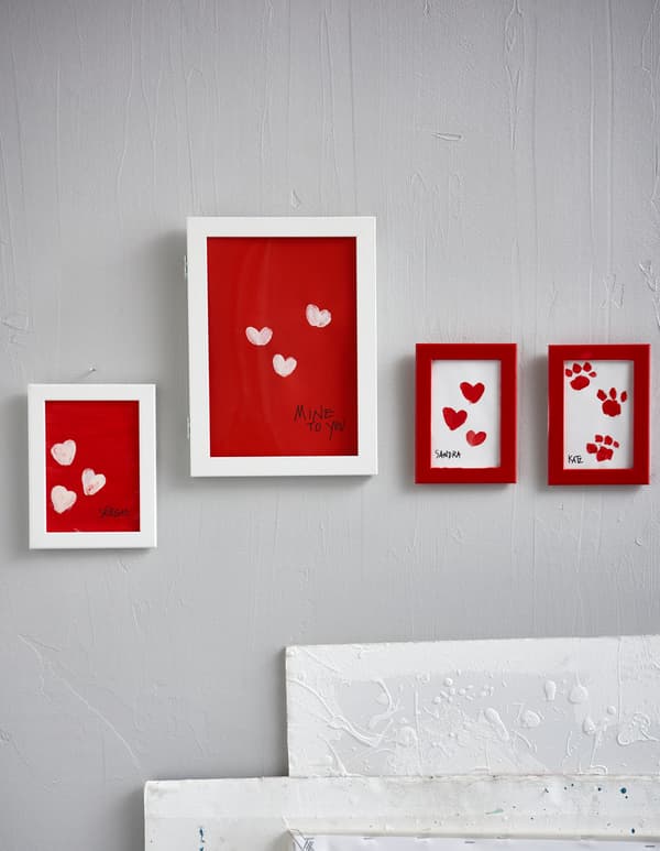 White and red frames display handmade pieces of art on a wall.