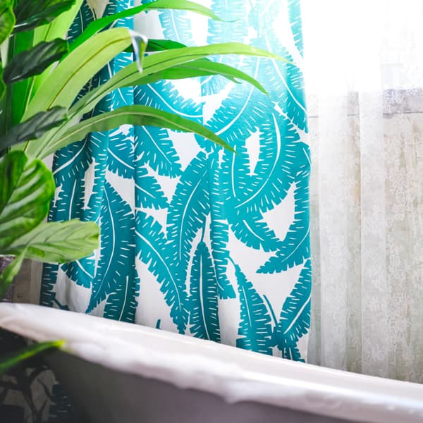 White and turquoise printed fabric is used as a shower curtain around a white bath. A plant is placed next to the bath.