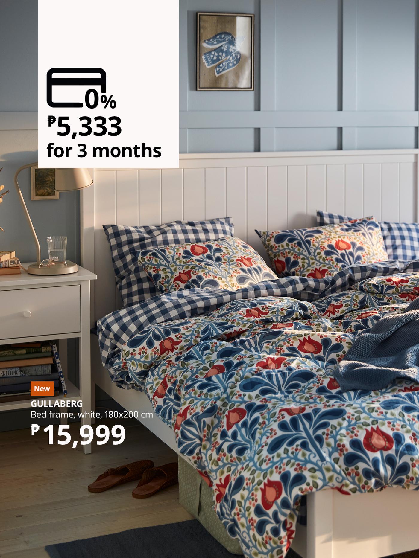 White bed frame with striped pillows, a dark gray blanket, two black lamps, and a nightstand in a modern bedroom. Price tag and installment details are displayed in the image.