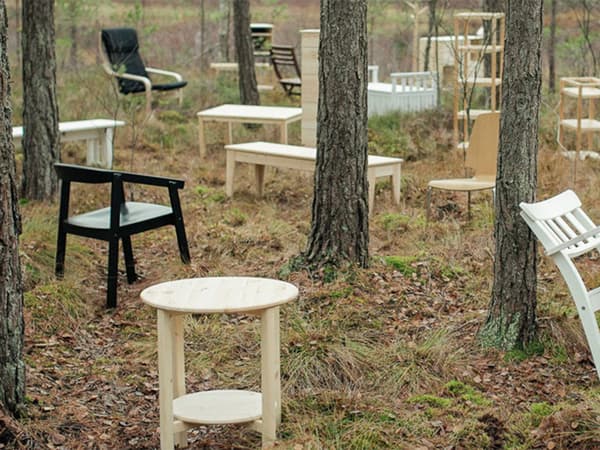 White, black, and light wooden tables and chairs scattered throughout a forest, one source of our renewable materials.