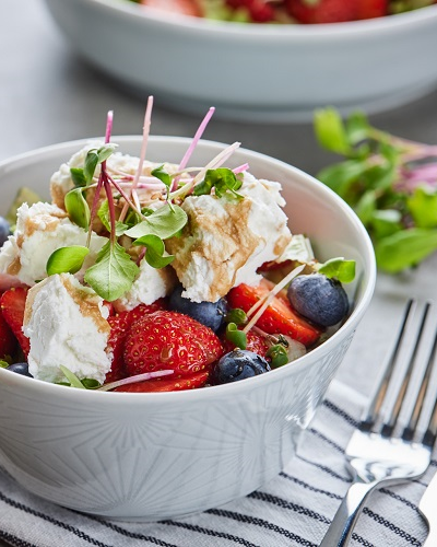 White bowl of salad with goat cheese and strawberries