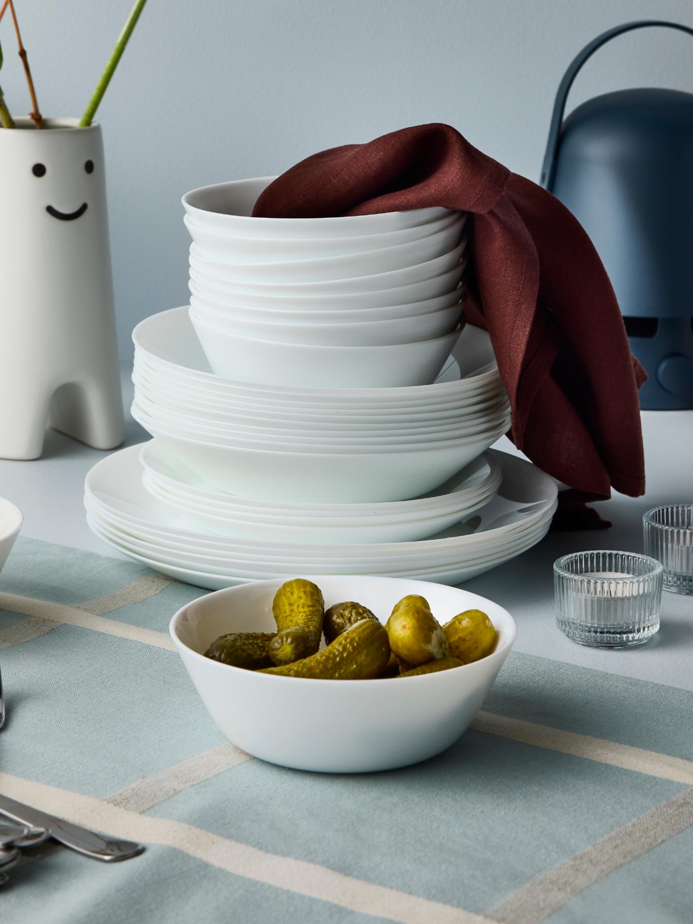 White bowls and plates from the OFTAST series are placed on a table, some of them stacked, and there are two FRÖVÄXT vases.