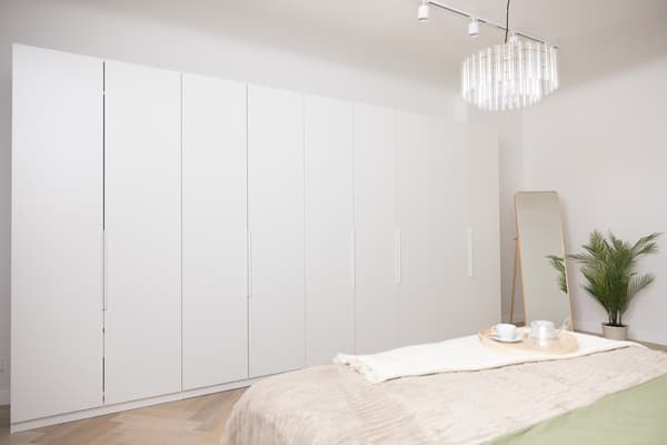 White built-in wardrobe with smooth doors in a bedroom, creating a bright and visually light space.