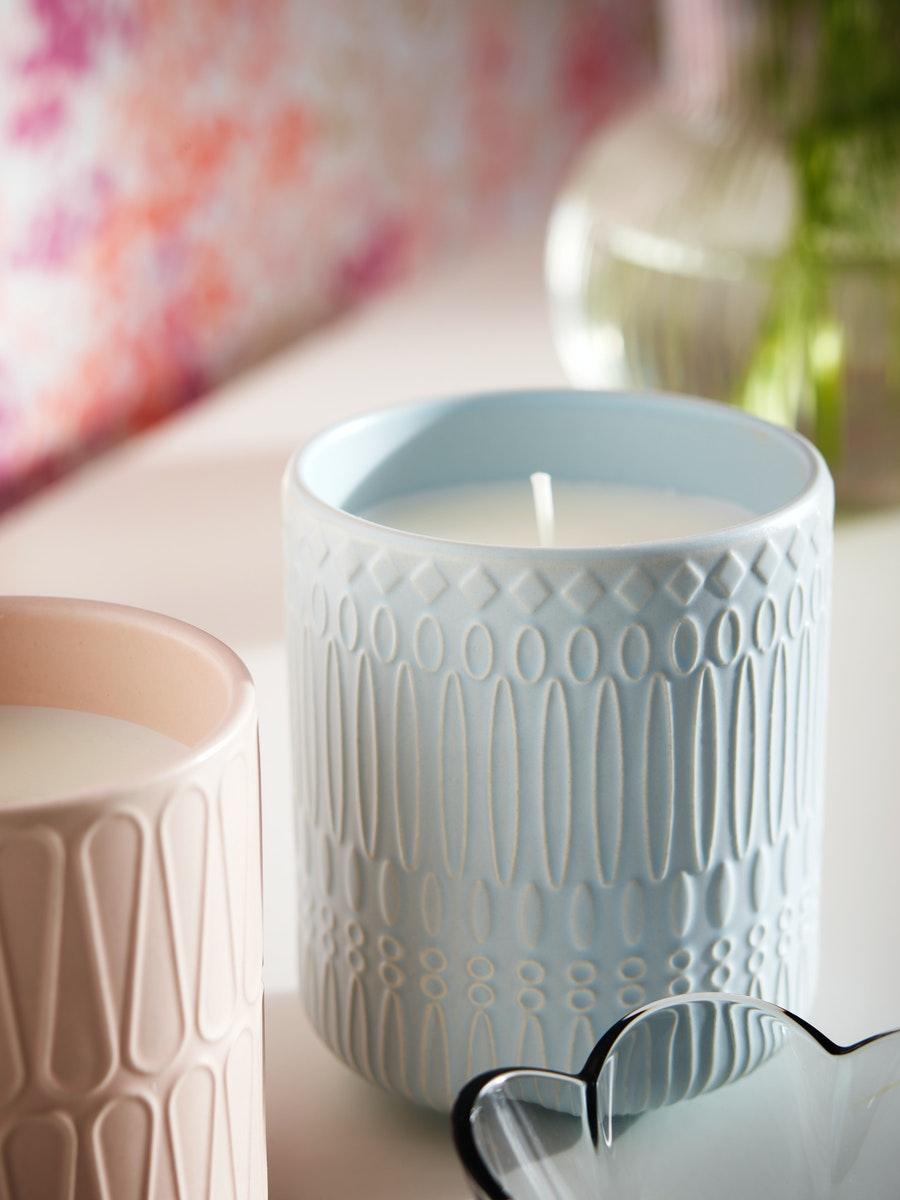 White ceramic candle holder with lit candle placed on a soft surface with a blurred floral backdrop.