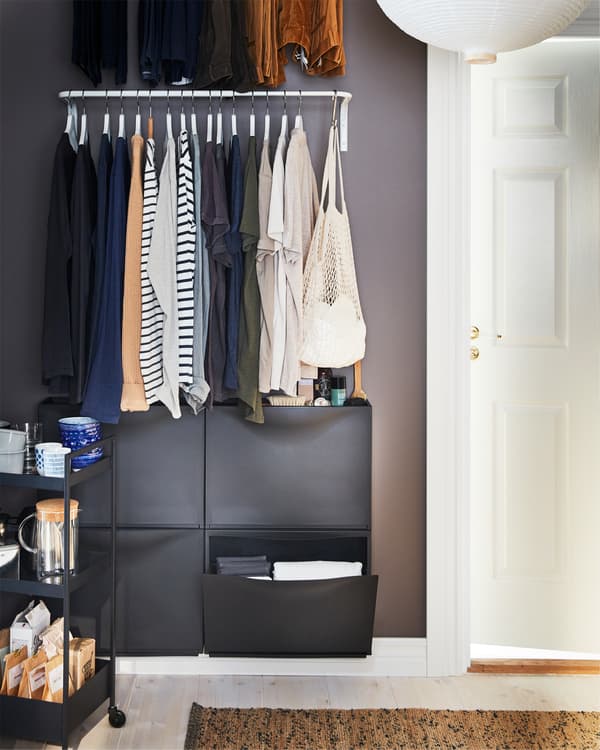 White clothes bar mounted on a wall with hangers with clothes, black wall-mounted shoe cabinets below and a black trolley.