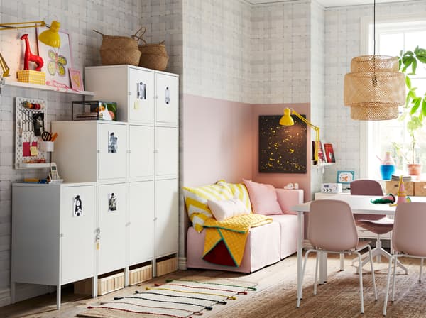 White HÄLLAN cabinets placed against a side wall and used for storage in a compact pink, white and yellow family living space.