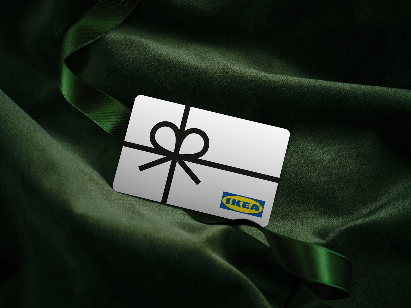 White IKEA gift card with a picture of a black ribbon on top of green velvet fabric.