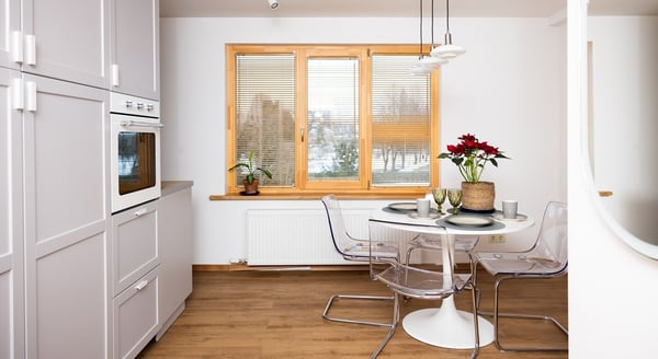 White kitchen and dining area with round table, transparent chairs, and large windows.