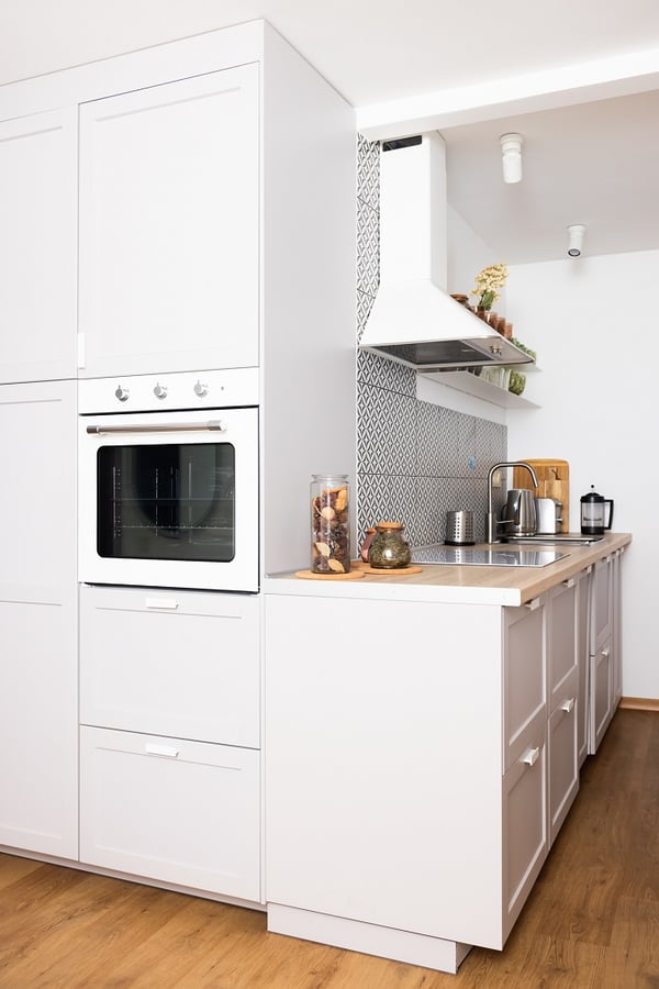 White kitchen cabinets with built-in oven and patterned backsplash.