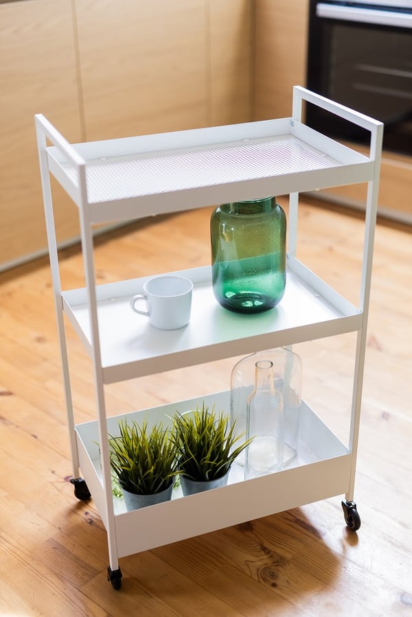 White metal kitchen trolley with plants, glass bottles, and minimalist decor