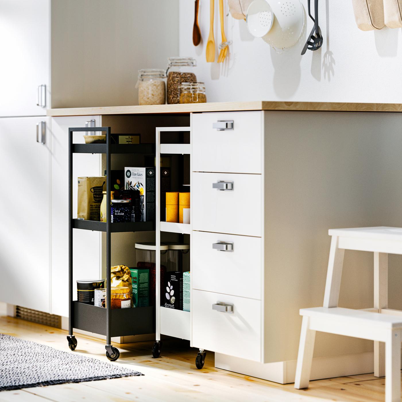 White METOD base cabinets and an EKBACKEN worktop with NISSAFORS trolleys – a black and a white – in a recess below.