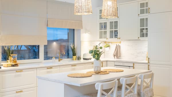 White modern kitchen with island, large window, and hanging wicker lights.