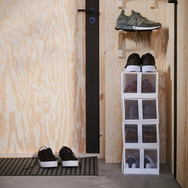 White narrow shoe boxes are stacked on a narrow wall next to a door. Above the boxes are brackets that store more shoes.
