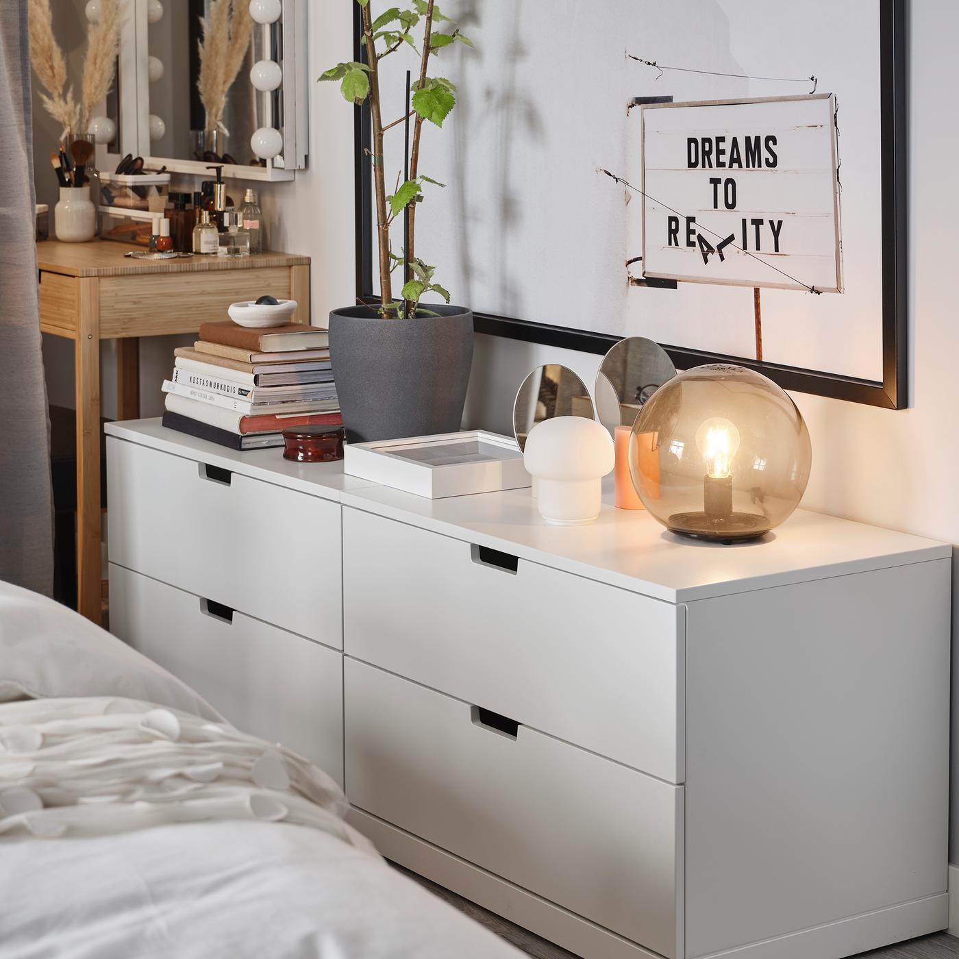 White NORDLI chest of drawer with a lamp, a plant and some books