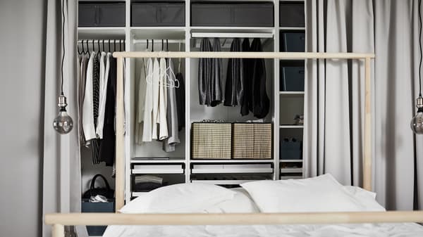 White PAX closet combination with several compartments holding different clothes, behind a bed with a white comforter.