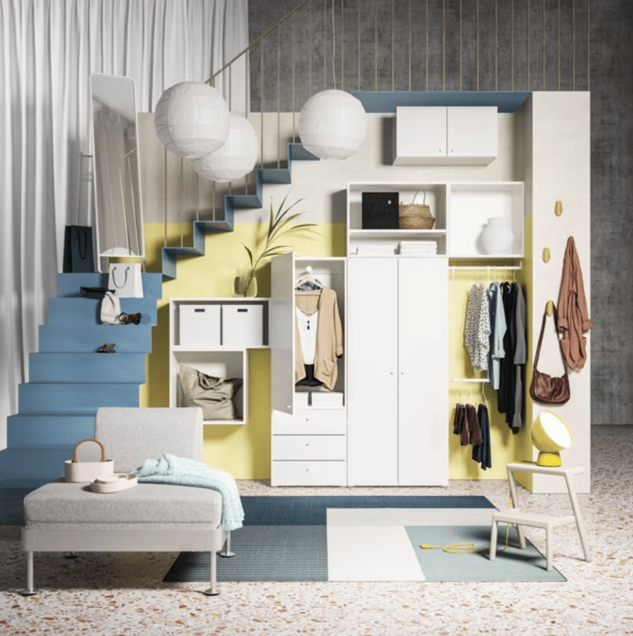 White PAX wardrobe against a light-green wall, two hinged doors open, shirts hang on a rail above drawers and a mesh basket.