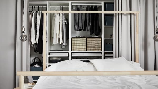 White PAX wardrobe combination containing different sections with multiple clothing items behind a bed with white duvet.