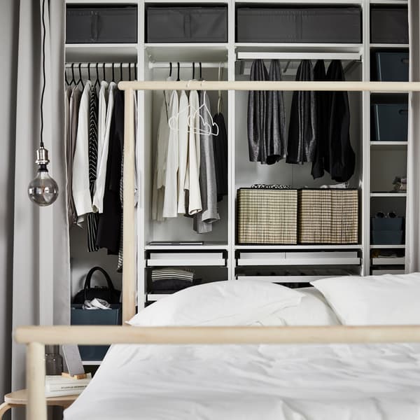 White PAX wardrobe combination with multiple sections that contain various clothes and boxes, behind a bed with white duvet.