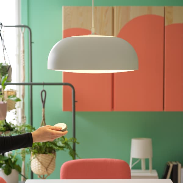 White pendant lamp and a hand that holds a TRÅDFRI remote control to demonstrate the dimming function.
