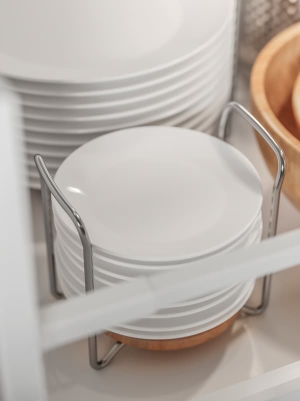 White plates stacked on top of each other and held in place inside a VARIERA plate holder made from stainless steel and wood.