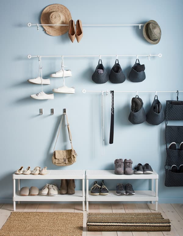 White rails hang on a wall above two shoe racks, and store hanging baskets and shoes.